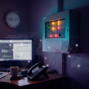 On‑call‑niche i en lille dansk virksomheds teknikrum ved nat: vægpanel med amber alarm‑LED, vægur, telefonhåndsæt og purpur/indigo belysning — symbol på en natlig driftshændelse og SLA‑risiko.