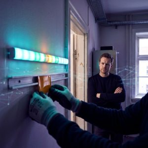 Tekniker sætter et farvekodet incident-flag under en vægmonteret SLA-LED-strip mens virksomhedsejer står i døråbningen og overvejer beslutning — cyan/grøn lys, ét amber blink.