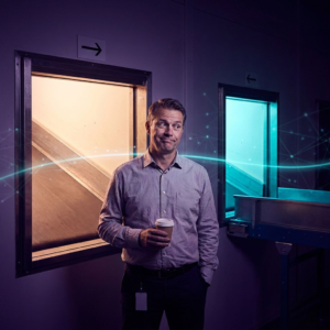 Operationsleder står ved en gate i et dansk baglokale; to gulvbaner fører henholdsvis mod en åben dør (hurtig handling) og en cyan‑oplyst verifikationsbane (søg/afstå). Deep purple/indigo stemning med cyan signalaccents, subtile data‑pulse overlays.