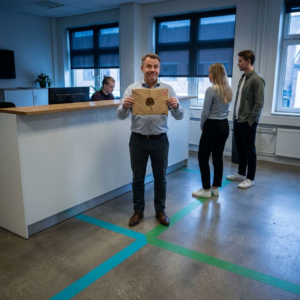 Nordisk pressefoto: kort kø ved advokatkontorets ekspedition, jurist modtager forseglet kuvert; cyan og grøn bane på gulvet som metafor for routing