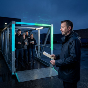 Nordisk pressefoto: en dansk operationsleder ved en serviceluge med en kort kø foran; åben gang til venstre og midlertidig afspærring til højre, aftenlys i indigo og cyan/green accenter.