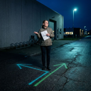 Aftenbillede af en dansk SMV‑lokation ved et datacenterindgangsparti: indigo skygger, cyan/grønne refleksioner i våde fliser, en lukket seddelbog og en foldet faktura i forgrunden — stemning af beslutningspres mellem pris og drift.