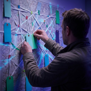 Beslutningsøjeblik i en mellemstor virksomheds operationsrum: en CTO foran et vægkort med deployment-ruter, deep purple/indigo stemning og cyan-grønne accenter, subtile datapulse-overlays.