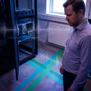 IT‑driftsleder i en dansk virksomhed foran markerede gulvbaner (cyan/green) der symboliserer netværkssegmentering; nordisk, indigo‑tonet operationsscene.
